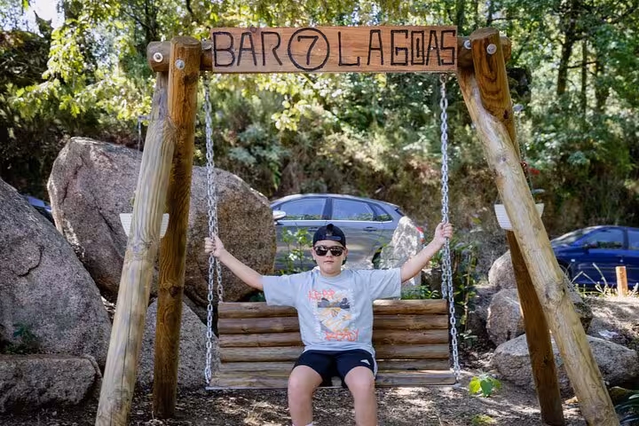 Young boy enjoying a swing at Bar 7 Lagoas, a popular rest stop in Geres National Park, surrounded by natural scenery.