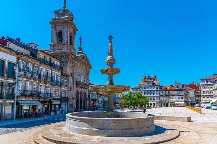 Braga's picturesque square with a stunning historic fountain, charming buildings, and clear blue sky on a sunny day.