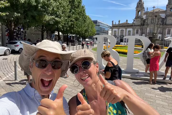 Happy travelers giving thumbs up at the Braga letters near the cathedral on a self-guided scavenger hunt