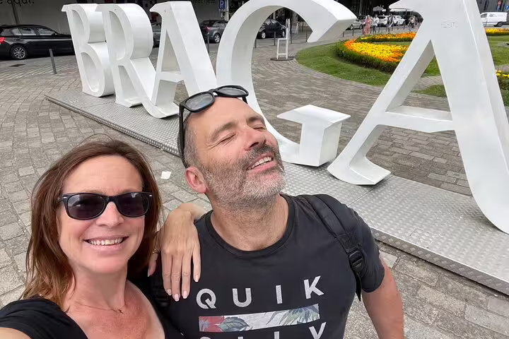 Smiling pair at the Braga sign on a self-guided scavenger hunt, sightseeing the city center landmarks