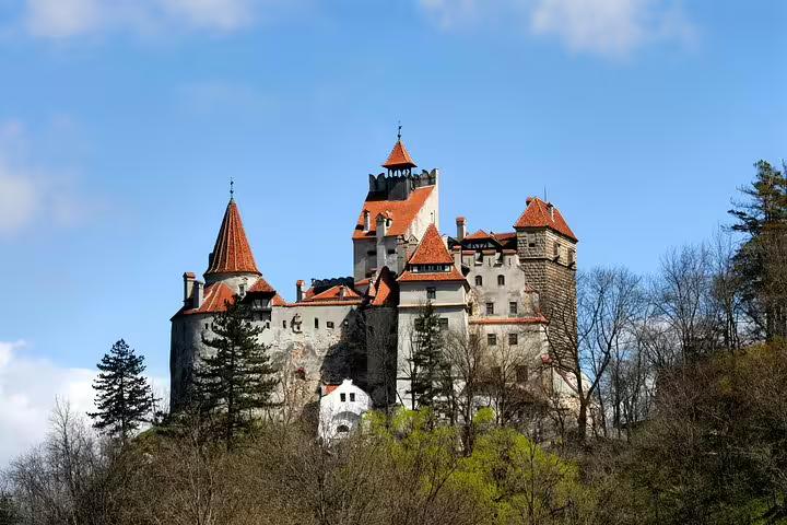 Bran Castle perched on a rocky hill with red-roofed towers and turrets surrounded by trees, Transylvania, Romania