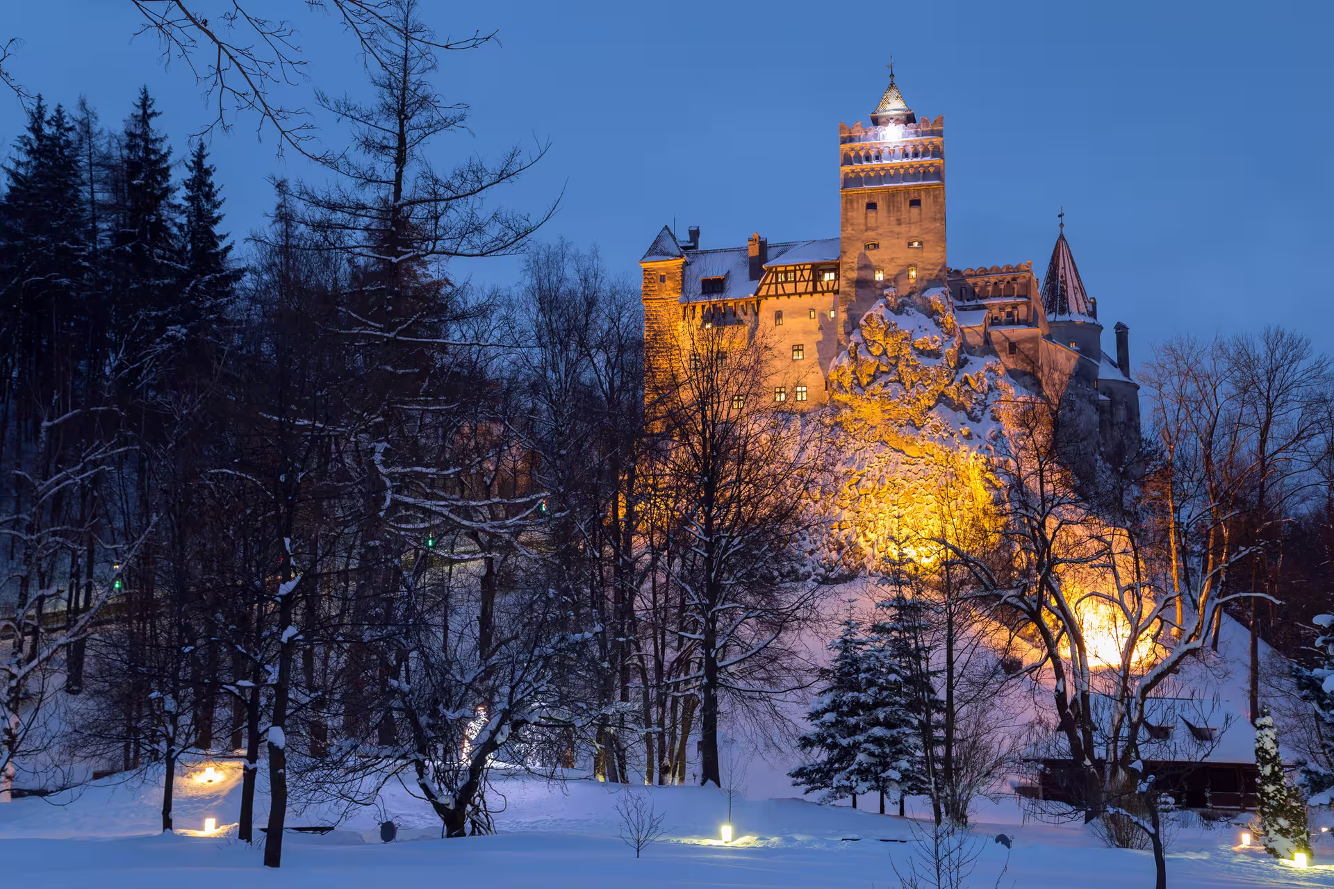 Bran Castle illuminated at dusk, surrounded by a snowy landscape, offering a magical winter experience in Romania.