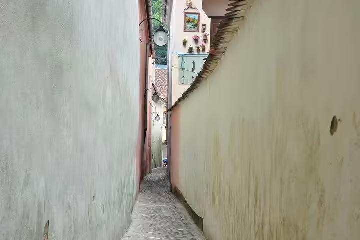 Narrow cobblestone alley between old pastel-colored walls in Brasov Old Town historic district
