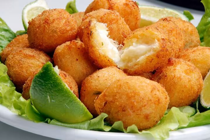 Crispy Brazilian cheese balls, known as bolinho de queijo, served with fresh lime wedges and lettuce.