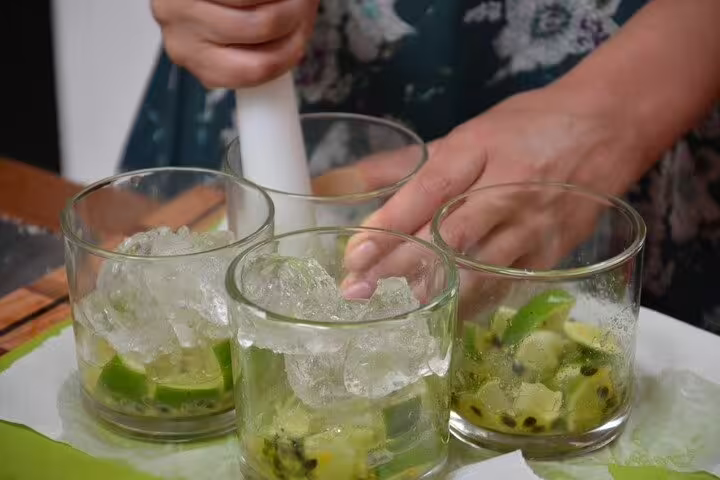 Hands preparing traditional Brazilian caipirinhas with lime and ice during a cooking class in Rio de Janeiro.