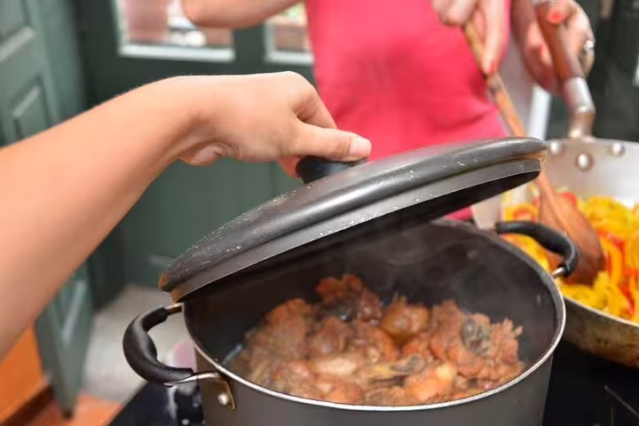 Participant lifts lid off simmering Brazilian stew during a hands-on cooking class in Rio de Janeiro.