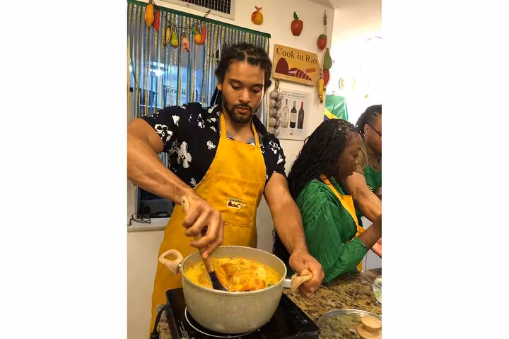 Man in a vibrant kitchen stirring a pot of Brazilian moqueca during Rio's Cookin' Good culinary class.