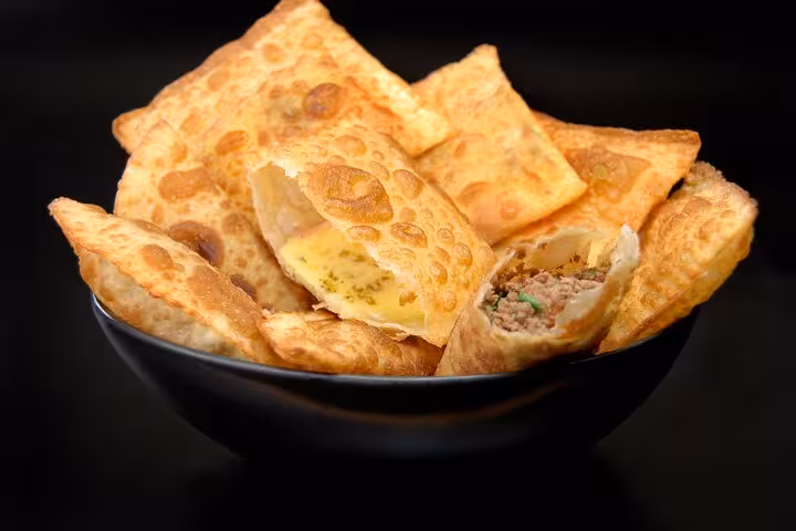 A bowl of freshly made Brazilian pastel pastries filled with cheese and meat, featured in a Bahian culinary class in Salvador.