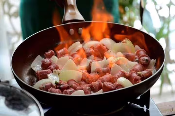 Sizzling Brazilian sausage and onion dish flambeed in a pan during a Rio de Janeiro cooking class.
