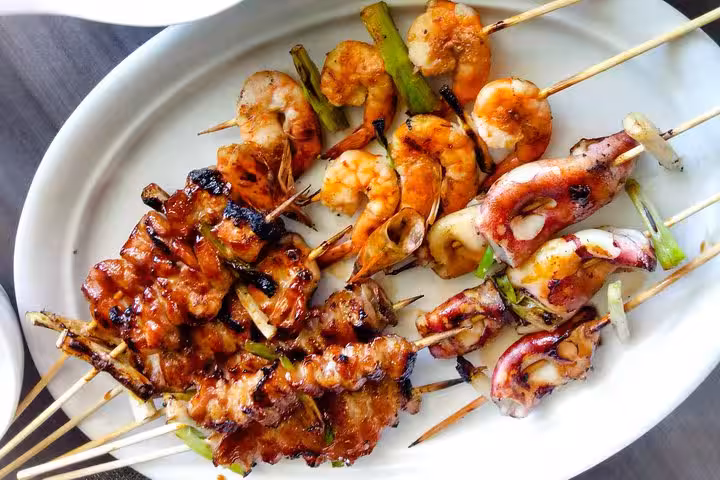 Assorted seafood skewers with grilled shrimp, octopus, and vegetables on a white plate for Rio cooking class.