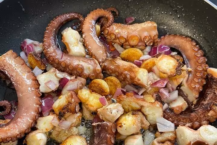 Sizzling octopus and garlic sautéed with onions in a pan, part of a vibrant seafood cooking class in Rio.