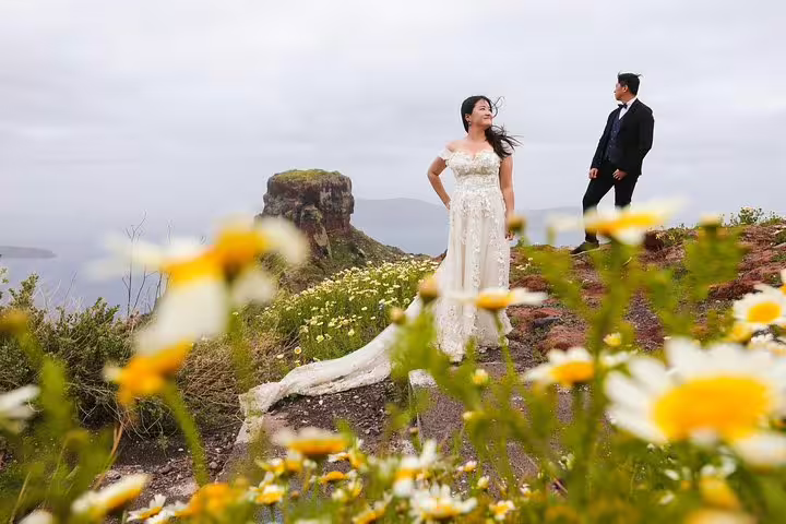 Bride and groom in a picturesque field of daisies overlooking Santorini's dramatic cliffs on a travel photography session.