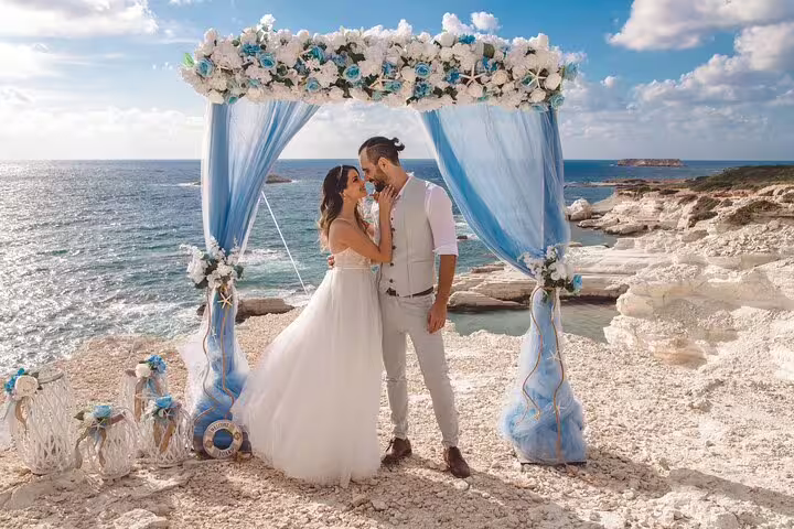 Bride and groom share a moment under a floral arch by the sea during a private photoshoot in Ayia Napa.