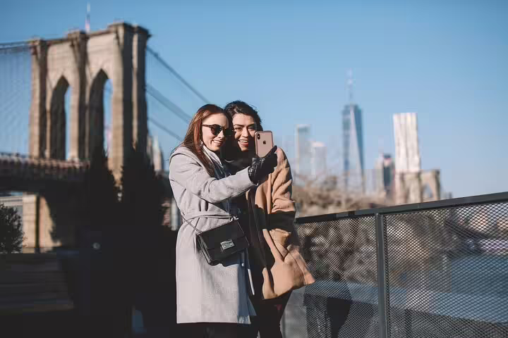 Friends taking a selfie with Brooklyn Bridge and NYC skyline, fun moment on Brooklyn & DUMBO photo walk