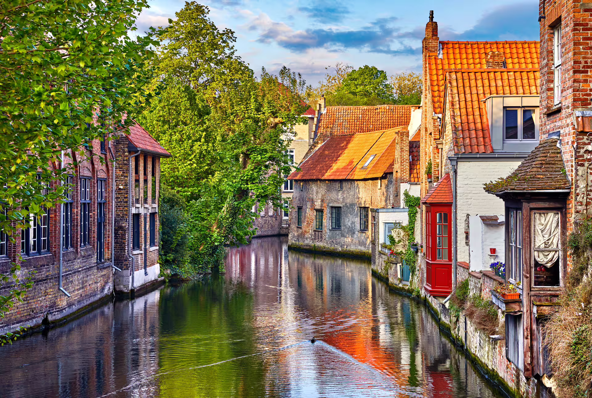 Peaceful Bruges canal with red-roofed houses and greenery, perfect for a 1-day walking tour audioguide