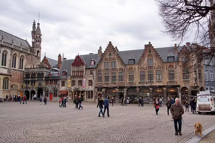 Tourists explore the historic Market Square with medieval architecture in Bruges on a private day trip from Brussels.
