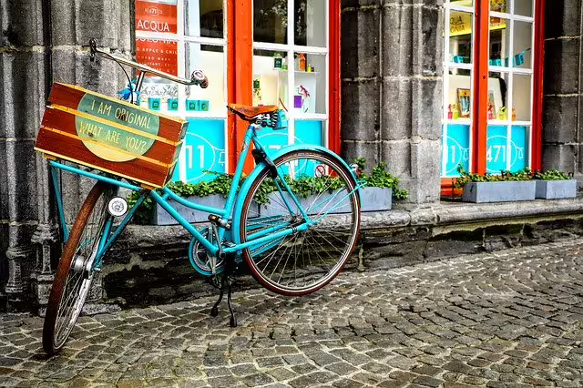 Vintage turquoise bicycle with a wooden sign rests on cobblestone street in Bruges, capturing the charm of a Flanders walking tour.