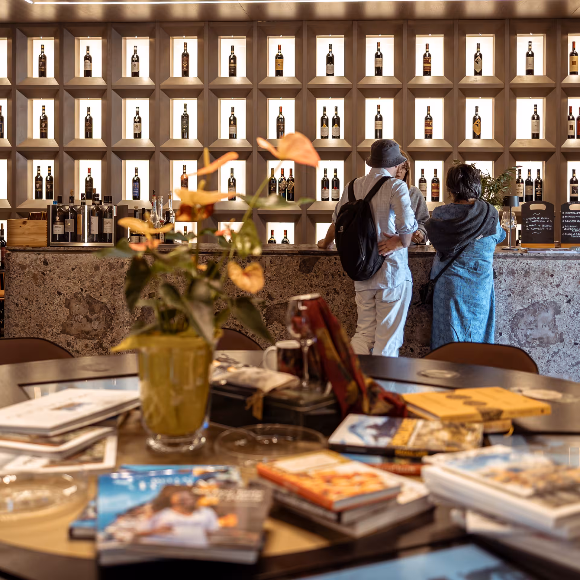Visitors exploring wine display at tasting room with vibrant floral decor in Pienza's renowned wine experience.