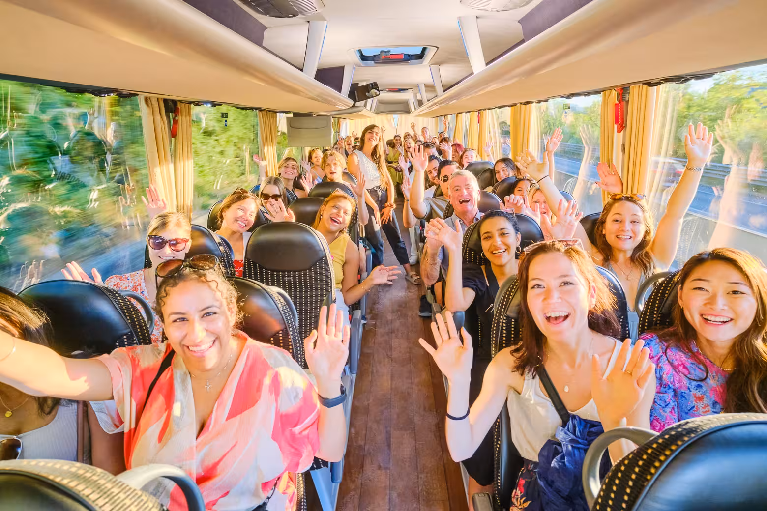 Happy tourists wave inside a comfortable bus on the Land of Brunello wine tour in Tuscany.