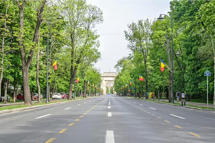 Tree-lined Kiseleff Boulevard in Bucharest with Romanian flags and triumphal arch in background