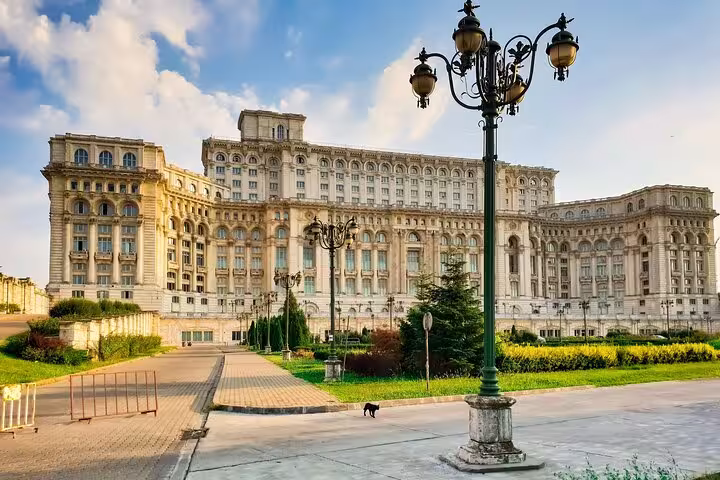 Front view of Bucharest's Palace of Parliament with lush gardens and ornate lampposts, perfect for a walking tour experience.