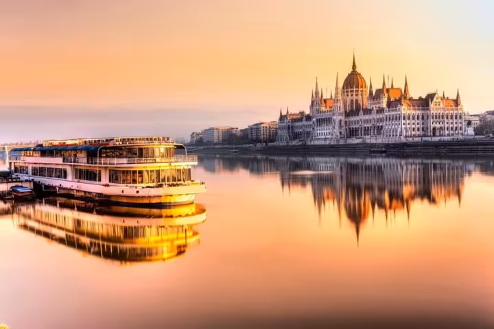 Danube river cruise boat with Hungarian Parliament at golden hour, Budapest day trip from Vienna small group