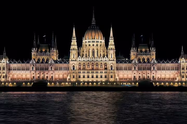 Illuminated Budapest Parliament building at night, reflecting on the Danube River, featured in a Vienna to Budapest day trip.
