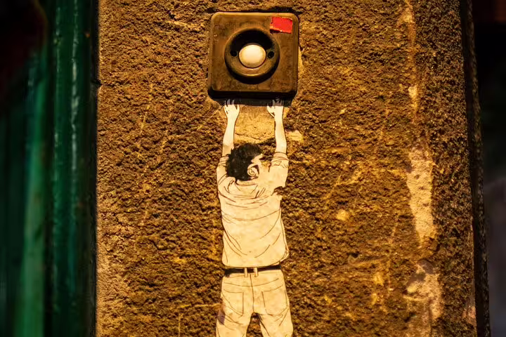 Budapest stencil of man reaching a doorbell on textured wall, quirky street art detail on walking tour