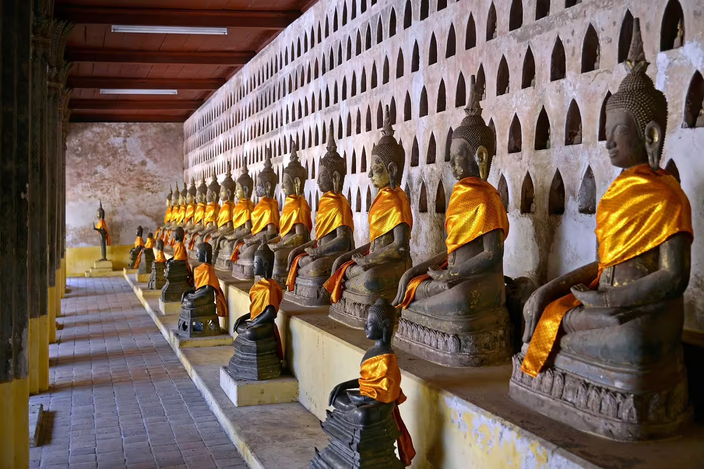 Row of Buddha statues draped in orange robes at a historic temple in Laos, reflecting cultural heritage.