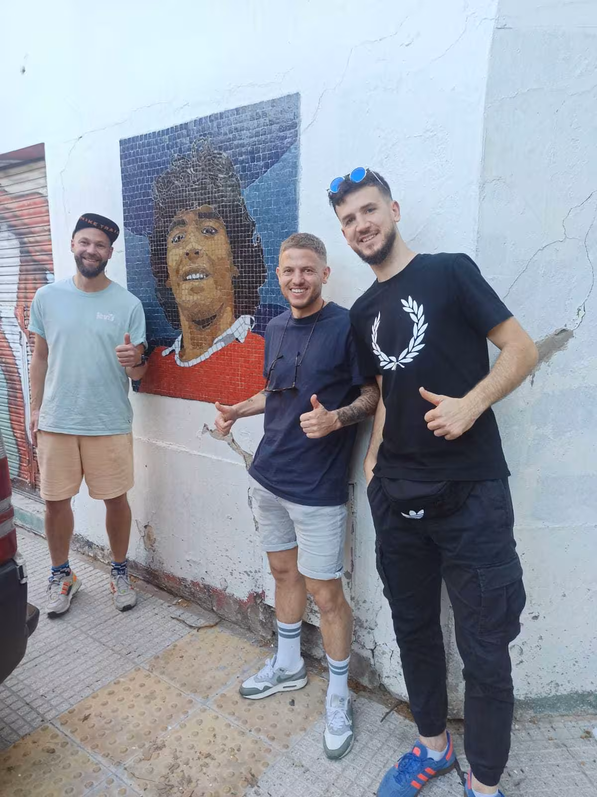 Tour guests pose by Diego Maradona street mural on Buenos Aires soccer matchday experience with a local