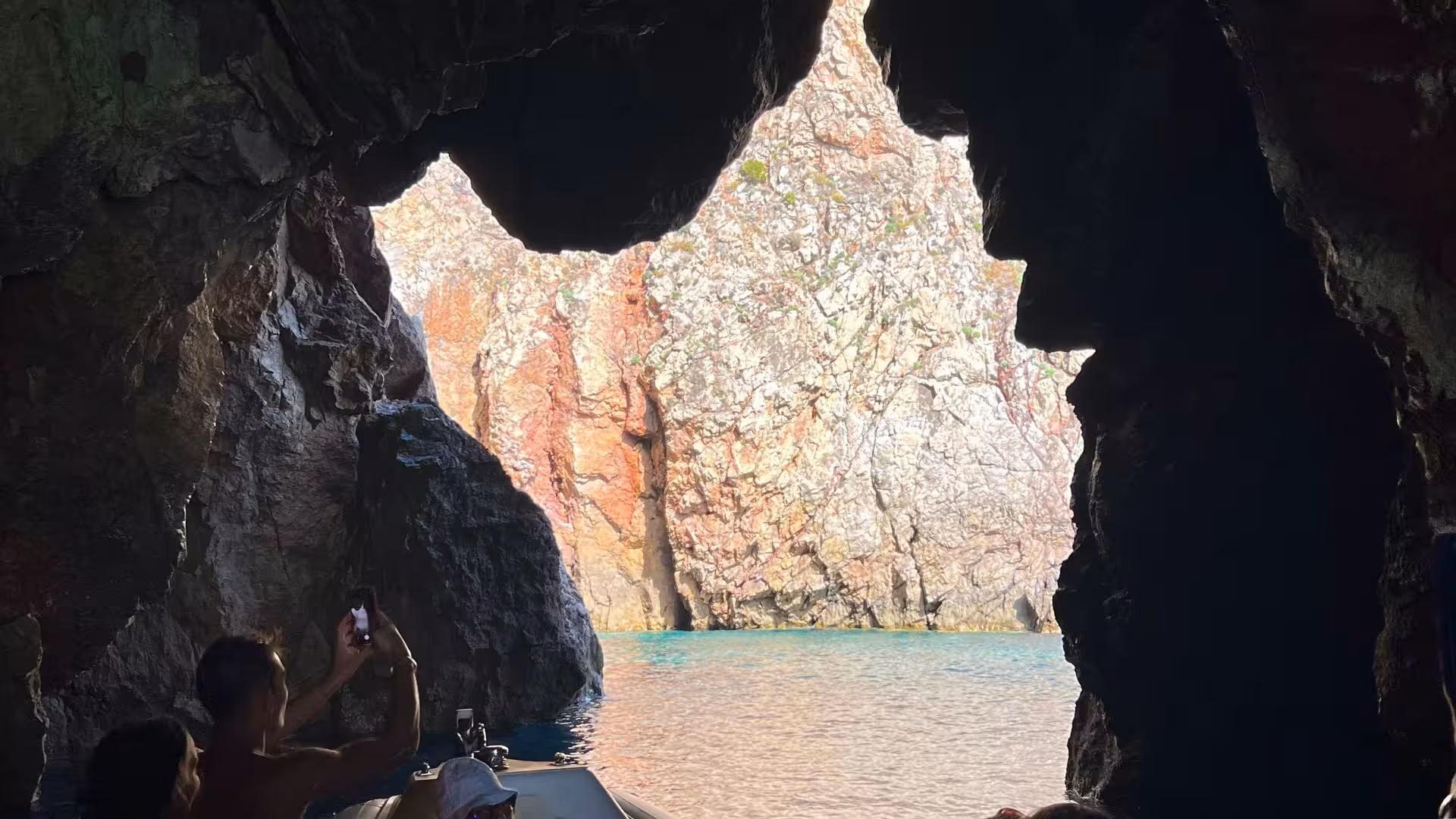 Tourists capturing the vibrant rock formations from inside a cave during a dinghy tour near Pan di Zucchero.