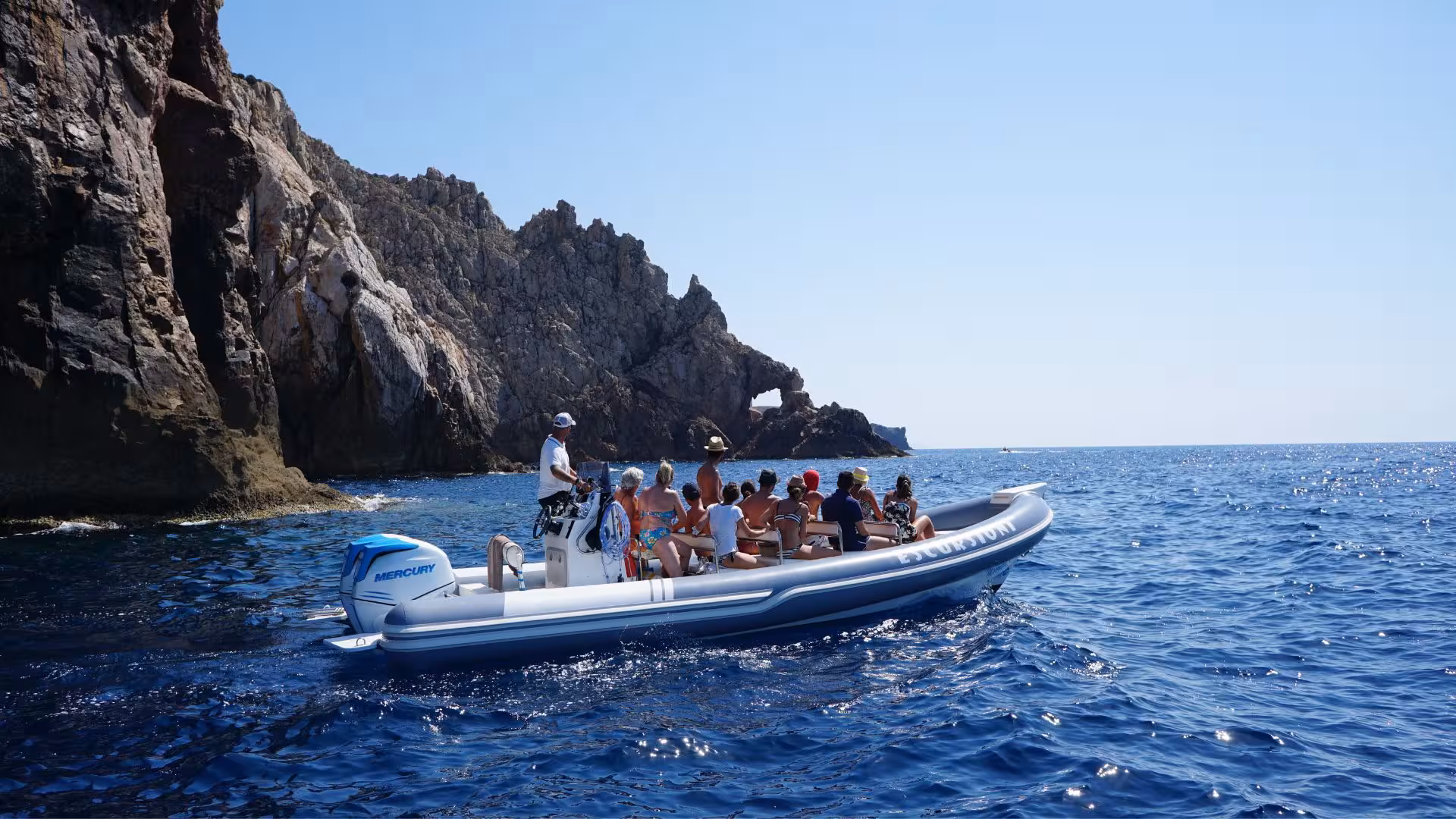 Group enjoying a scenic dinghy ride near rocky cliffs on the Pan di Zucchero and Porto Flavia tour from Buggerru.