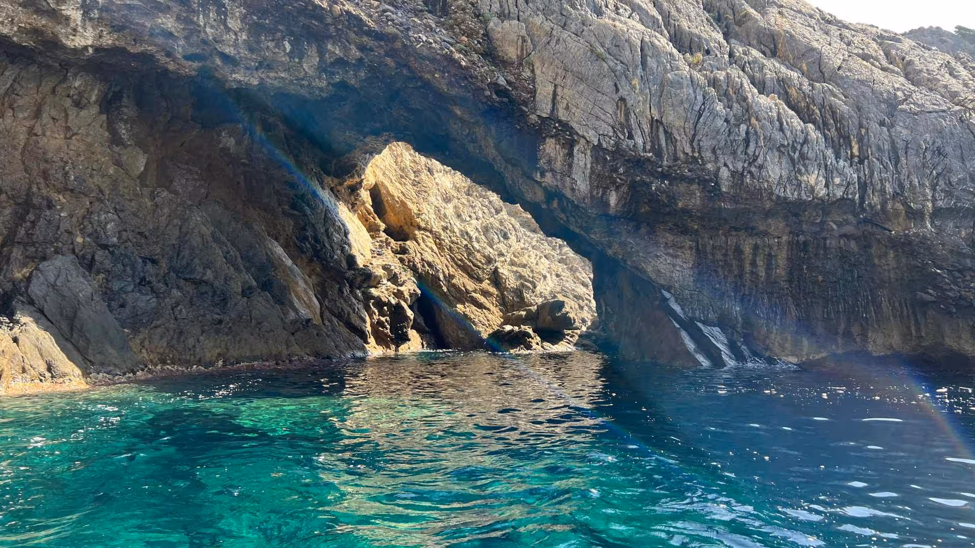 Sunlight illuminates the cave entrance and emerald waters on a Buggerru dinghy tour near Porto Flavia.