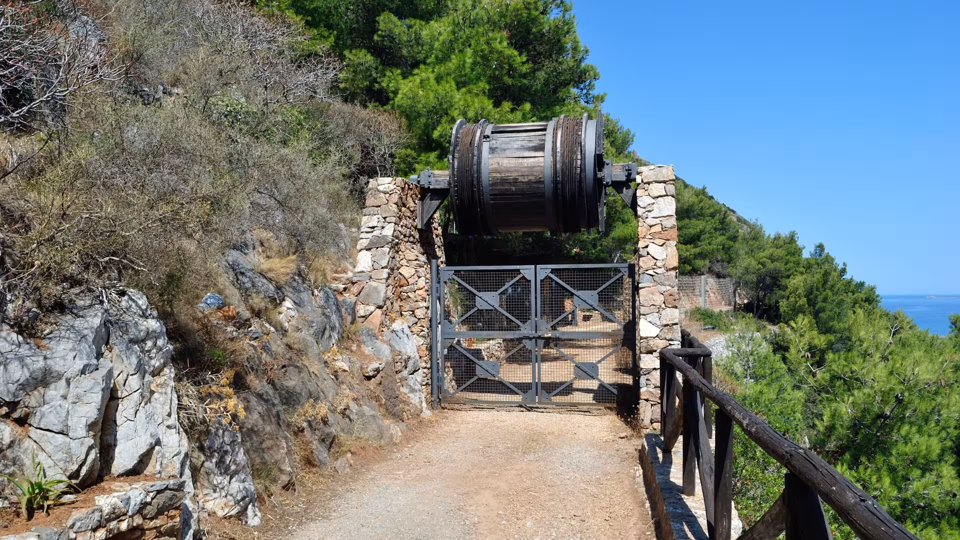 Entrance to Galleria Henry tunnel in Buggerru, Sardinia, featuring historic mining equipment and lush surrounding landscape.