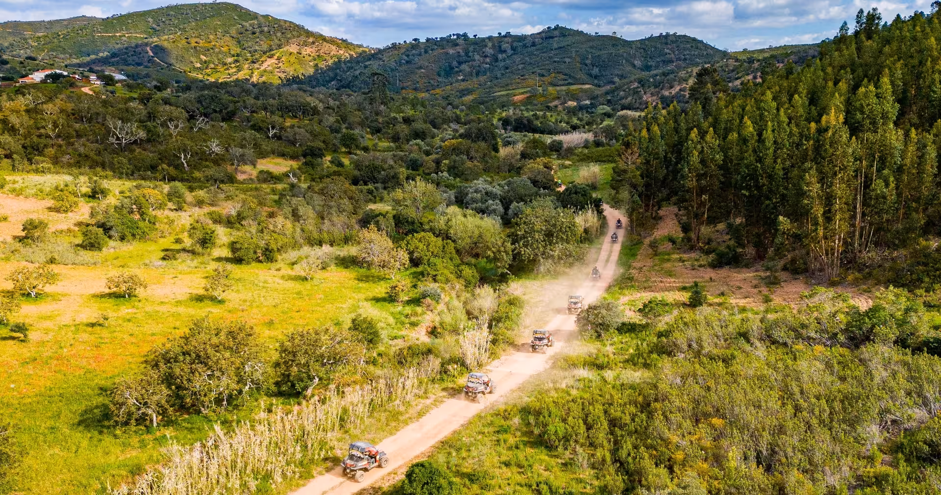 Convoy of buggies driving along a dusty track through lush Algarve hills and valleys on a guided half-day off-road tour