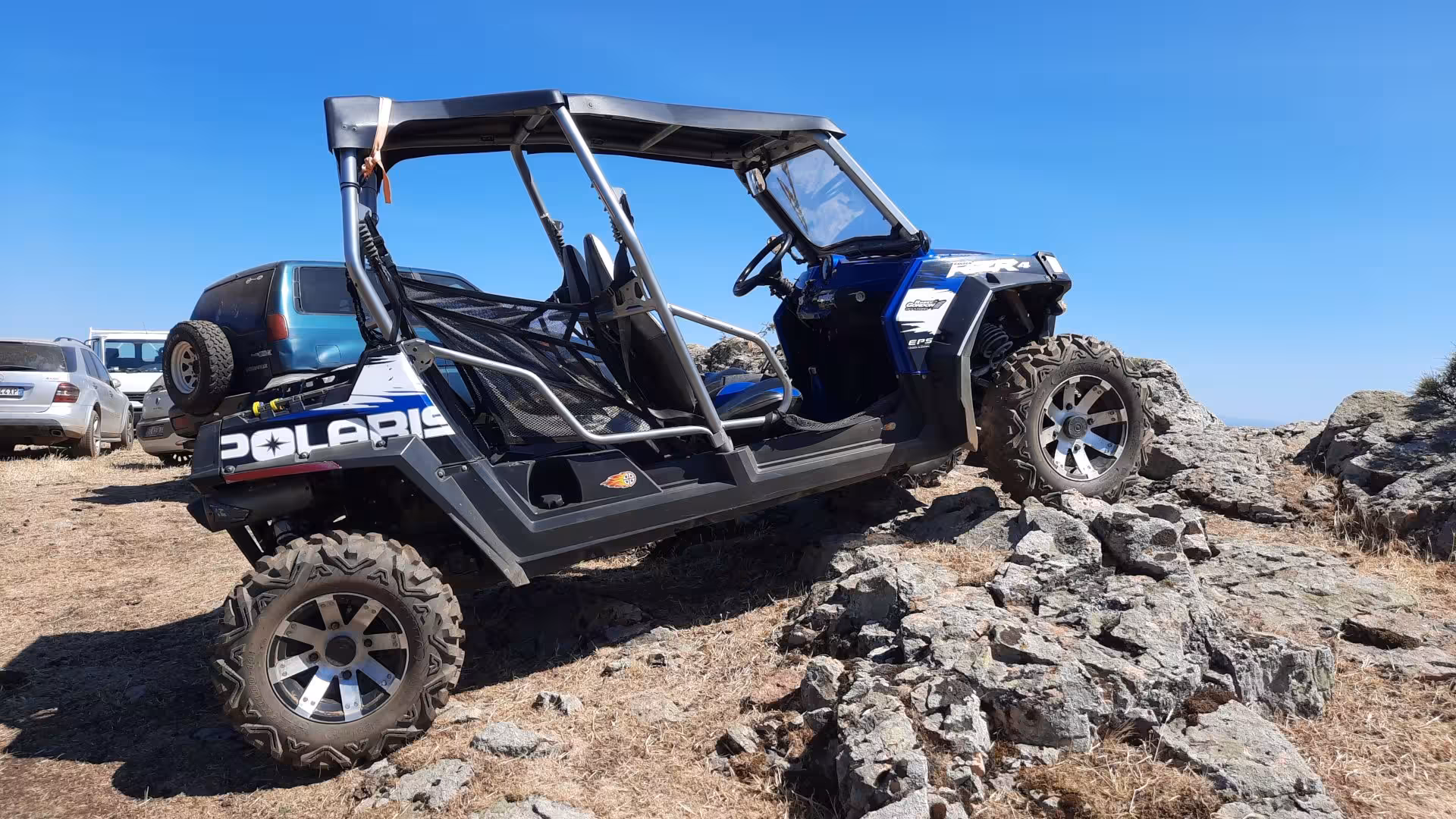 A buggy navigating rocky terrain with parked cars in the background on the Gennargentu buggy tour from Aritzo.
