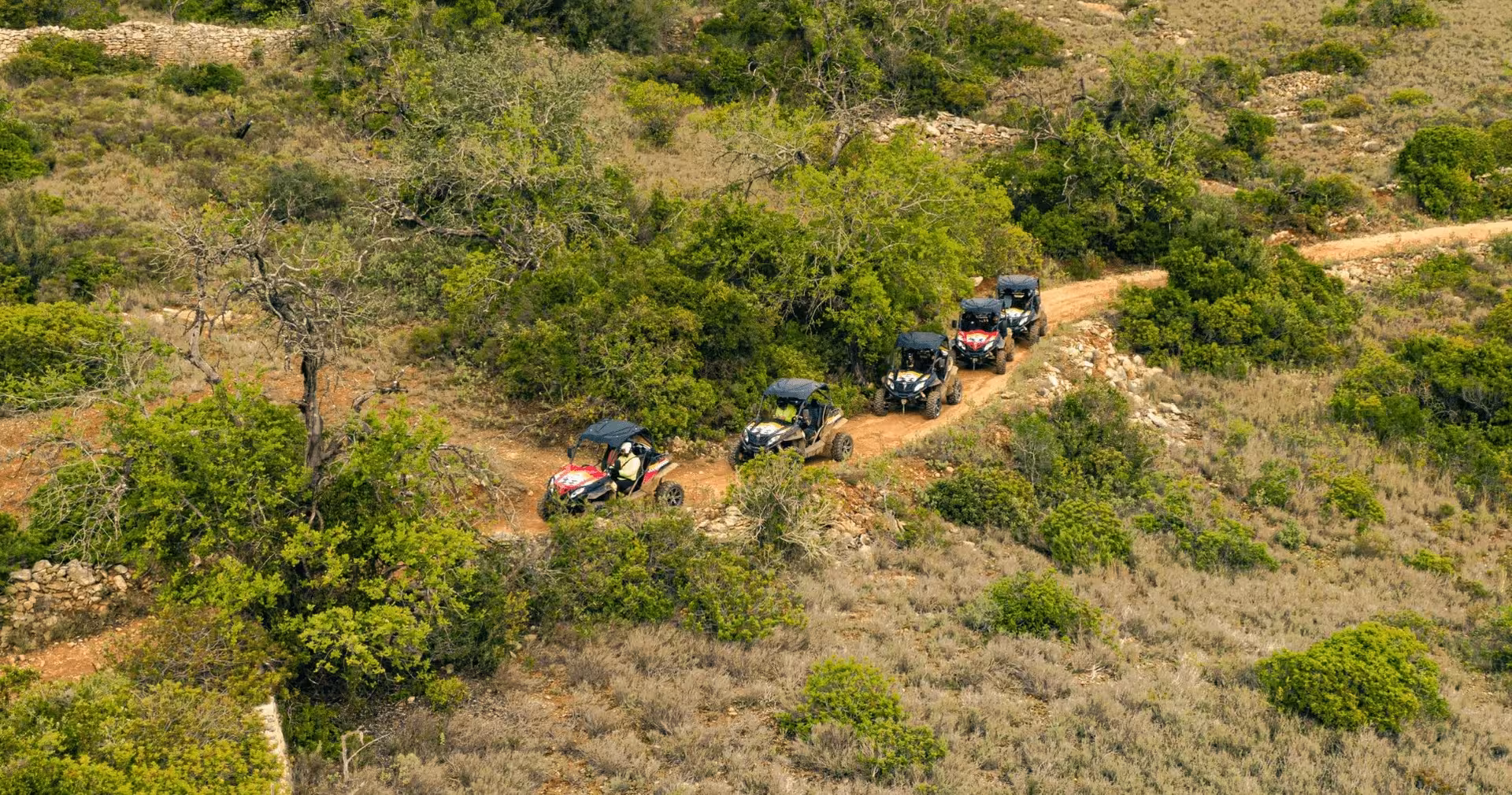 Convoy of off-road buggies driving along a rugged dirt trail through scenic Mediterranean countryside on a guided adventure tour