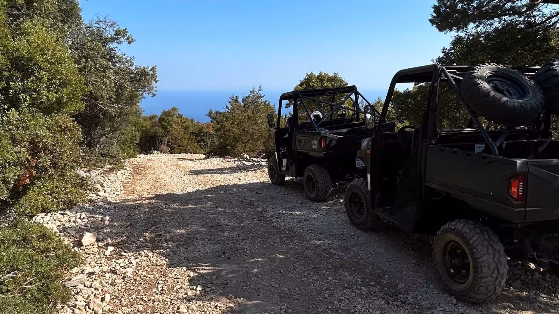 Off-road buggies on a rocky trail surrounded by greenery with a glimpse of the sea in the distance in Baunei.
