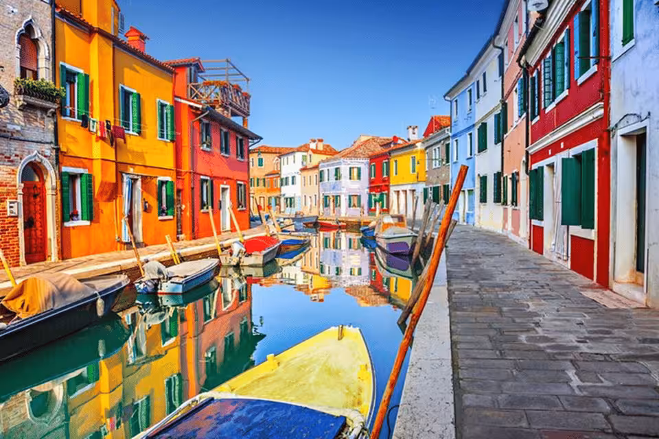Colorful houses and boats line the scenic canal in Burano, showcasing the island's vibrant charm and unique beauty.