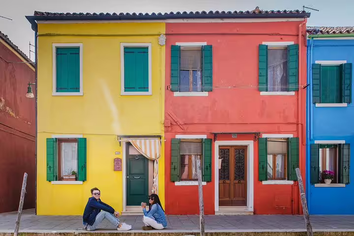 Colorful Burano houses with a couple sitting outside, highlighting the vibrant charm of the Grand Canal tour.