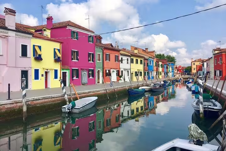Colorful Burano houses reflecting in a serene canal, a highlight of the Private LimoBoat tour through Murano and Torcello.