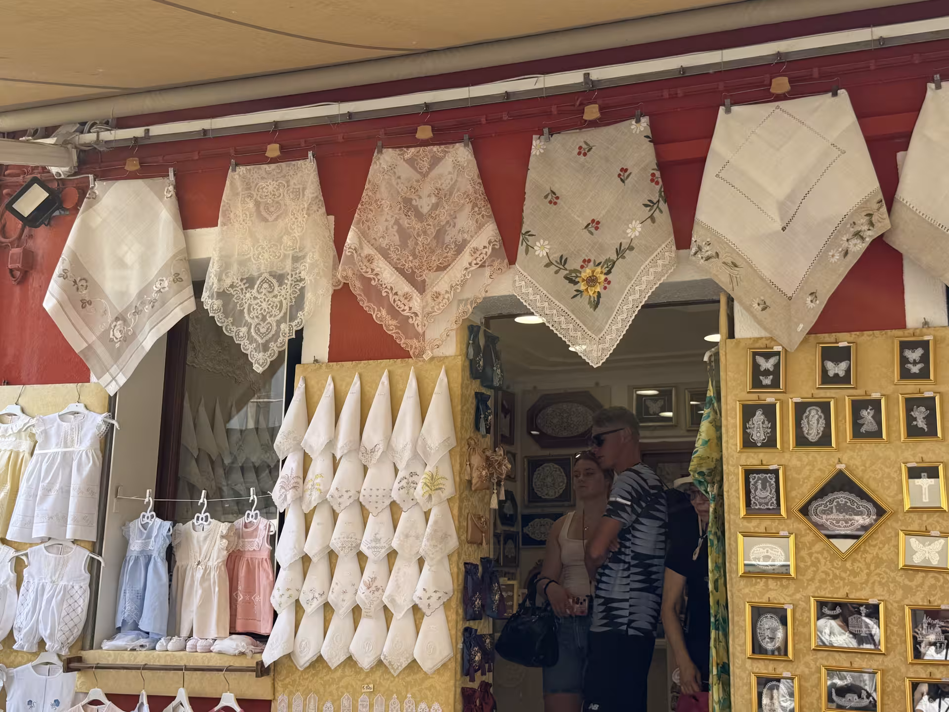 Colorful Burano lace shop displaying handcrafted linens and framed artwork, ideal for Venice cultural tours.