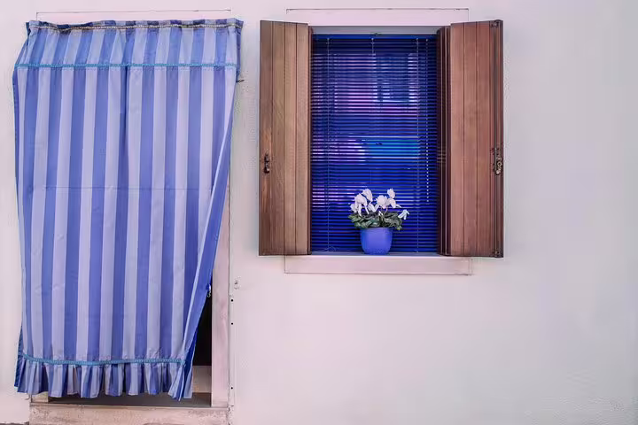 Charming Burano window with blue blinds and a potted flower, perfect for the Grand Canal Boat Private Tour.