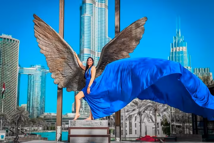 Woman in a flowing blue dress poses with angel wings against the iconic Burj Khalifa backdrop for a stunning Instagram shoot.