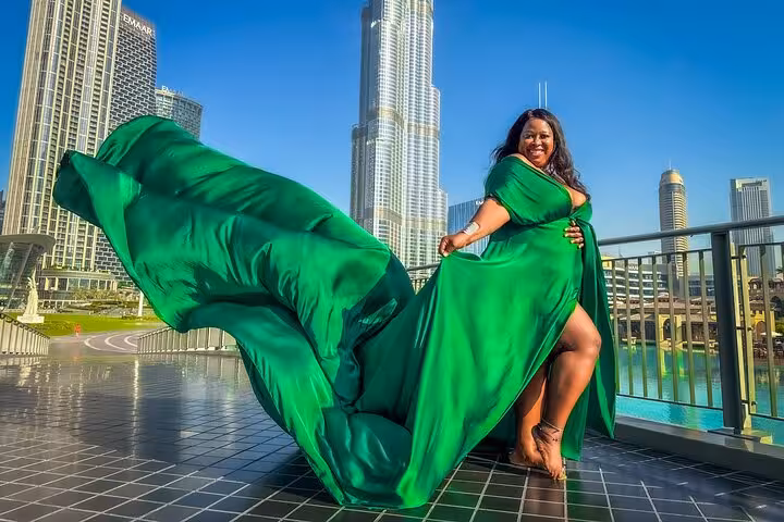 Smiling woman in a vibrant green dress with a dramatic train, set against the iconic Burj Khalifa, perfect for Instagram moments.