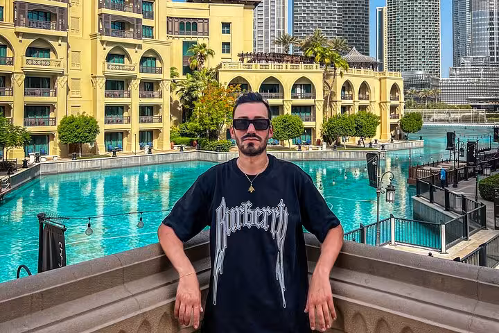 Man in sunglasses stands by a turquoise pool with Burj Khalifa in the background on an Instagram tour.