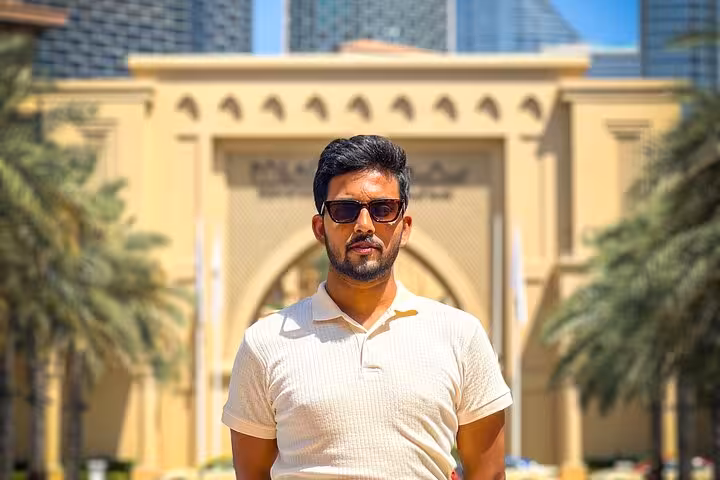 Tourist in sunglasses stands in front of a grand entrance with palm trees on a Burj Khalifa Instagram tour.
