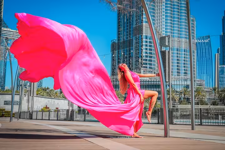 Woman in a flowing pink dress poses dramatically by Burj Khalifa, perfect for Instagram videography shoot.