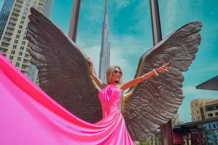 Woman in pink dress with angel wings poses at Burj Khalifa for Instagram videography shoot in Dubai.