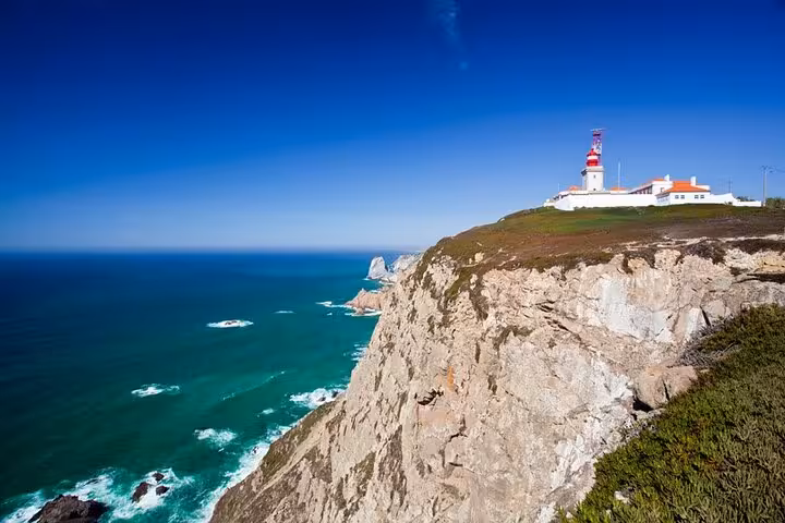 Cabo da Roca lighthouse perched atop dramatic cliffs with expansive ocean views on a sunny day during Sintra tour.